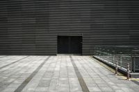 an empty square, with black vertical slats and silver stripes, is in front of a building with gray brick