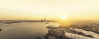 the sun is setting over a city by the water, as boats pass through it