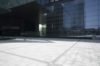 a sidewalk with stone tiles and a large mirror building in the background on a sunny day