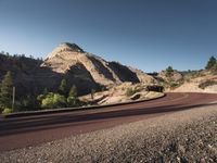 the lone, empty highway is lined with boulders and trees, as seen from across an open area