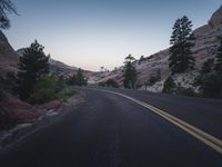 a lone road going uphill along a cliff side at dusk with the sun setting