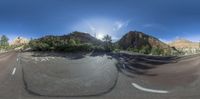 a 360 - camera photo of a road, with rocks in the background and some trees in the foreground