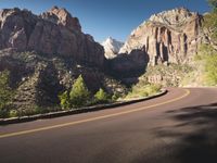 two people riding their bikes on a mountain road near cliffs of red rock mountains, near zion in zion, ut