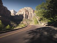 a bendy road through the wilderness with rocky cliffs in the background as viewed from a distance