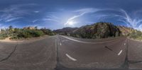 a 360 - panorama photo of a road in the desert near a mountain range on a cloudy day